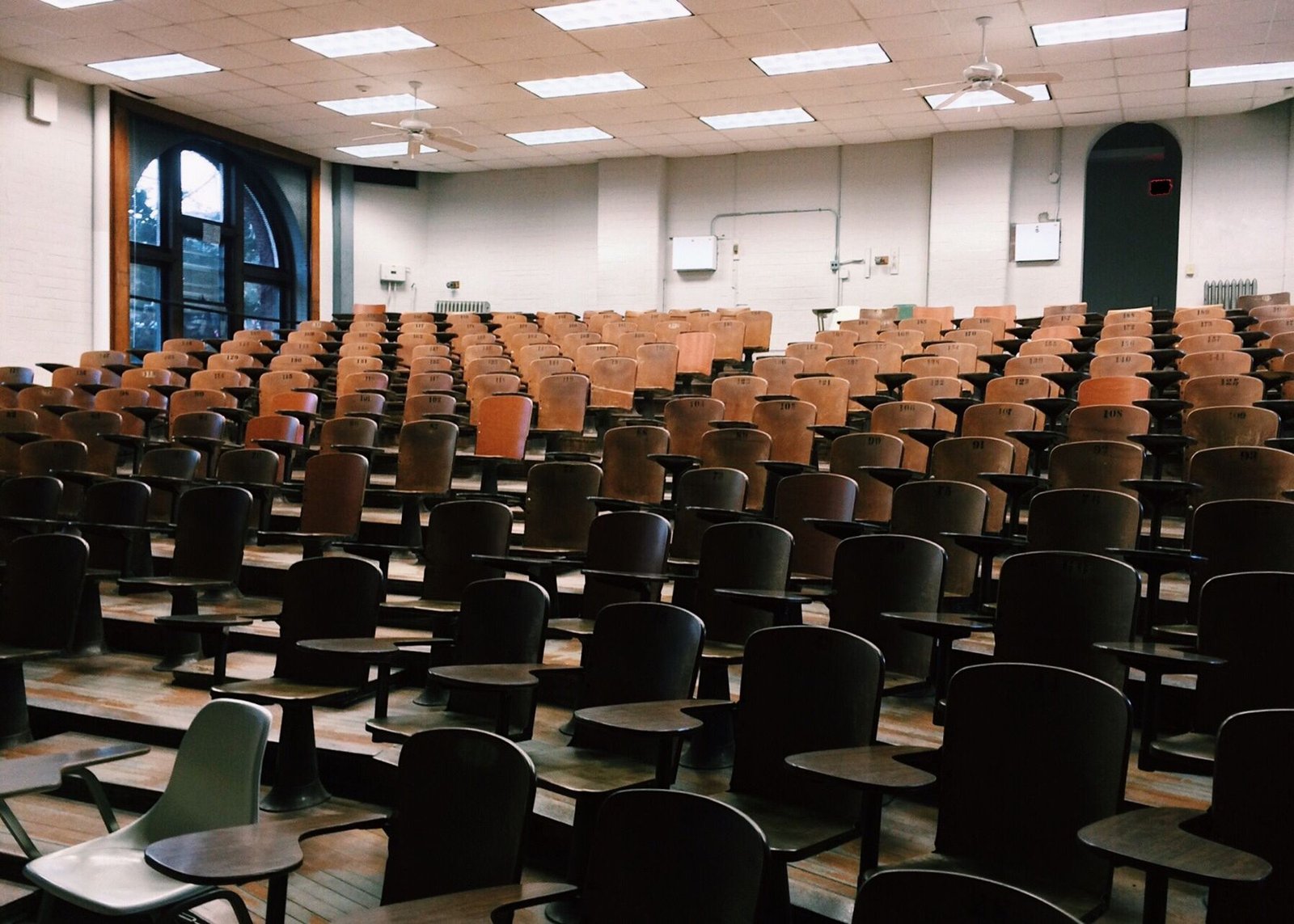 An empty tiered lecture hall with rows of wooden seats
