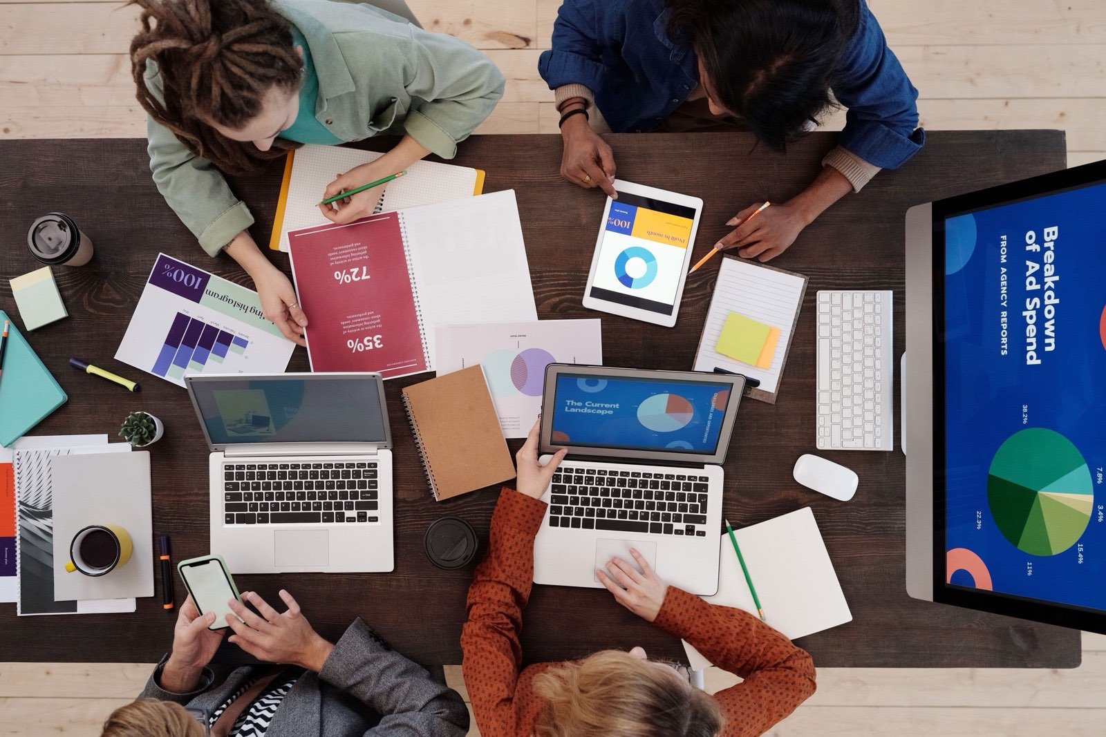 A marketing team working around a table of printed charts with an ad spend breakdown on screen