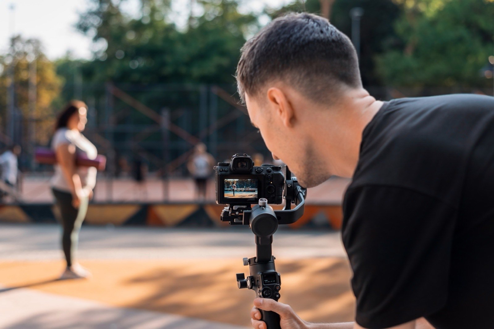 A videographer filming a subject on a gimbal-mounted mirrorless camera outdoors